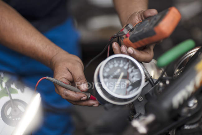Mecánico de motocicleta en el taller de celebración de un medidor de voltaje - foto de stock