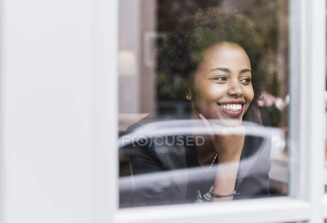 Souriant jeune femme regardant par la fenêtre — Photo de stock