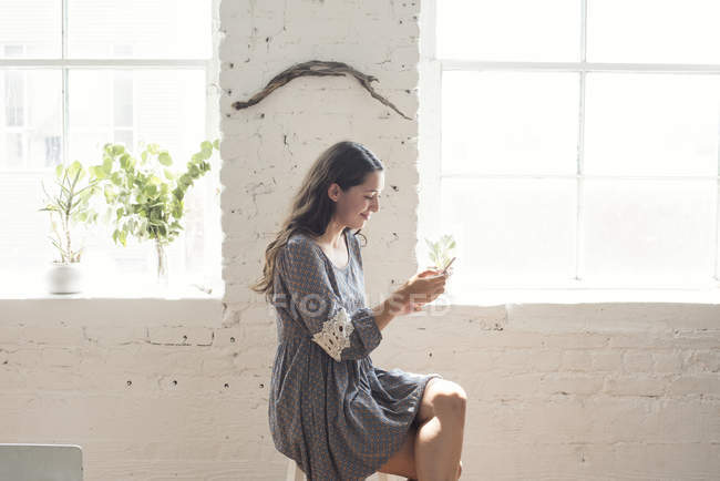 Усміхаючись молодої жінки, дивлячись на мобільний телефон в лофт — стокове фото