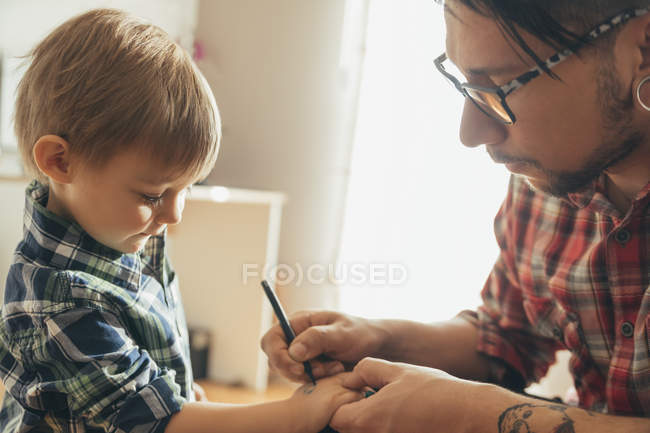 Padre pintura tatuaje en los hijos mano - foto de stock