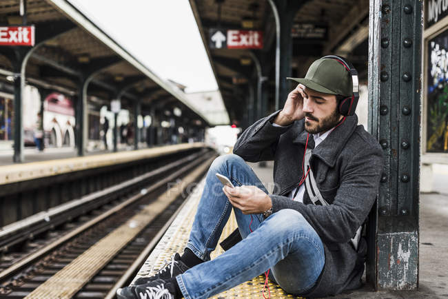 Junger Mann wartet mit Smartphone am Bahnsteig auf U-Bahn — Stockfoto