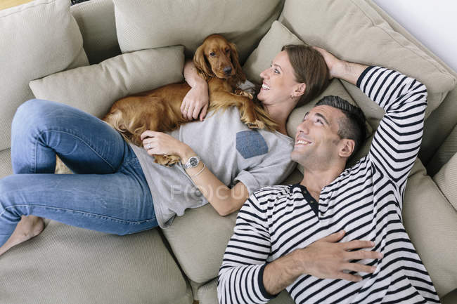 Smiling couple with dog lying on couch — Stock Photo