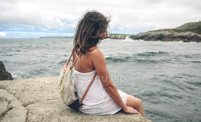 Frau mit Rucksack sitzt auf Seebrücke und blickt aufs Meer — Stockfoto