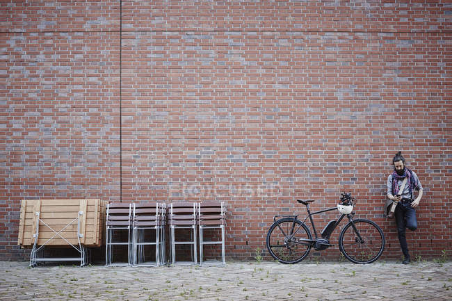 Portrait de cycliste à l'aide d'un téléphone portable près du mur de briques — Photo de stock