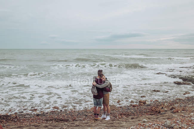 Pareja gay abrazándose en la playa en frente del mar - foto de stock