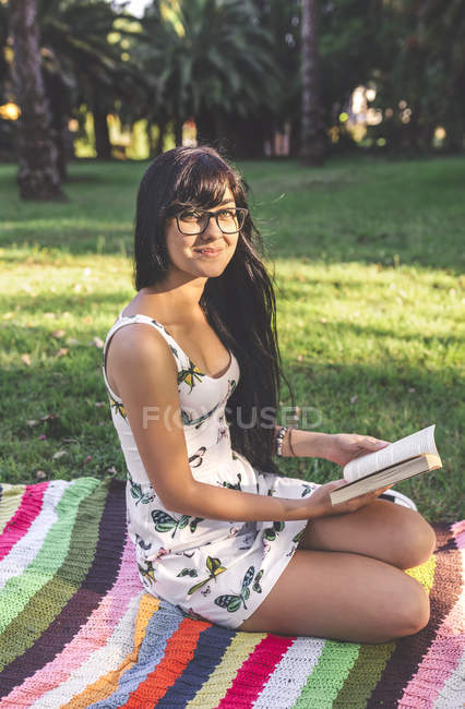 Молодая женщина, сидящая на одеяле в парке с книгой — стоковое фото