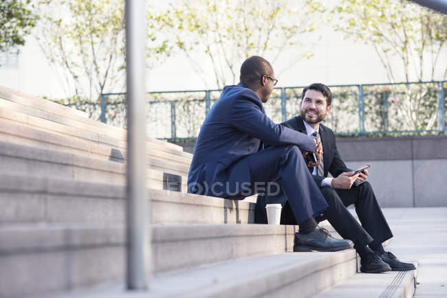 Two businessmen sitting on stairs and talking in city — Stock Photo