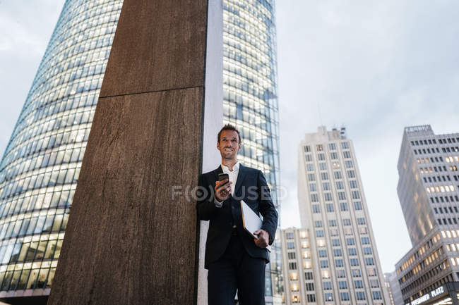 Allemagne, Berlin, Potsdamer Platz, homme d'affaires debout avec smartphone et ordinateur portable dans la soirée — Photo de stock