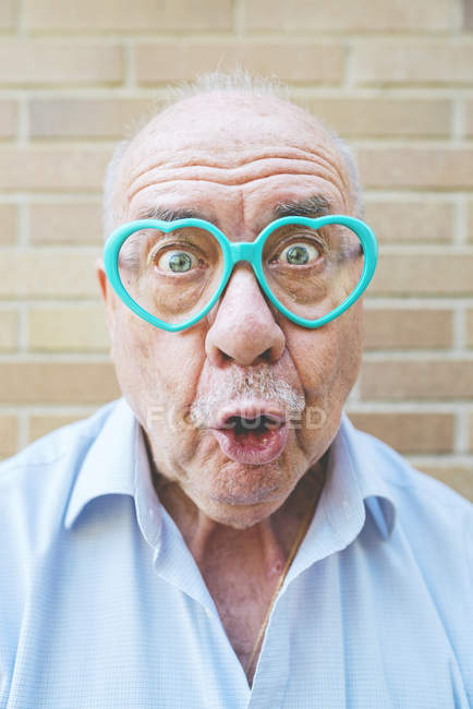 Ritratto di uomo anziano che indossa occhiali a forma di cuore tirando facce divertenti — Foto stock