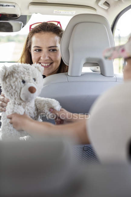 Mère regardant sa fille jouer avec un ours en peluche en voiture — Photo de stock