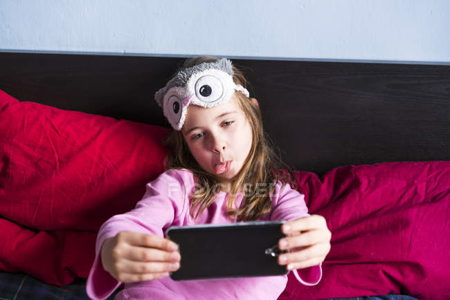 Girl лежачи на ліжку і беручи selfie з мобільного телефону — стокове фото