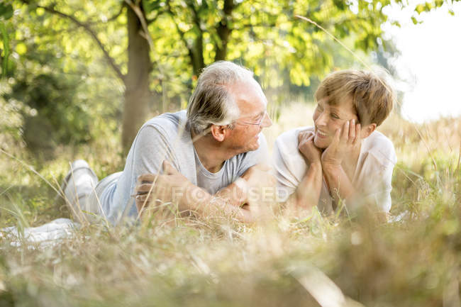 Pareja mayor acostada en un jardín soleado sobre una manta - foto de stock