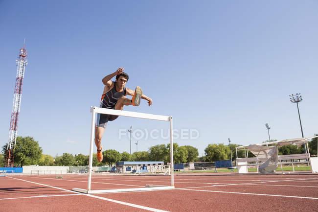 Athlete clearing hurdle during a race at stadium — Stock Photo