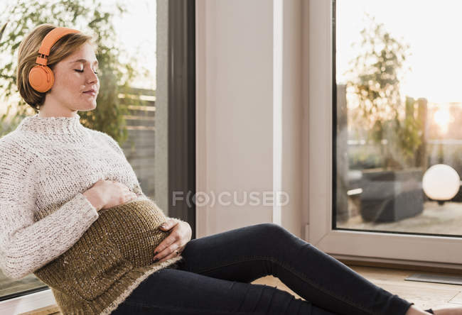 Pregnant woman sitting on floor and listening to music — Stock Photo
