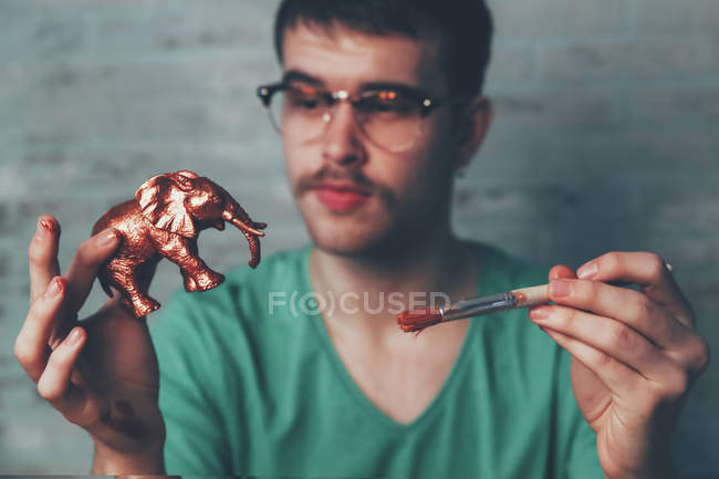 Young man painting plastic elephant figure with copper paint — Stock Photo