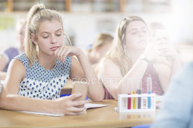Aburrido adolescente en la clase de química de la escuela secundaria usando el teléfono celular - foto de stock