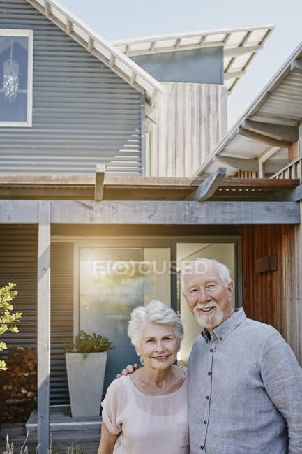Senior couple standing in front of house and looking at camera — Stock Photo