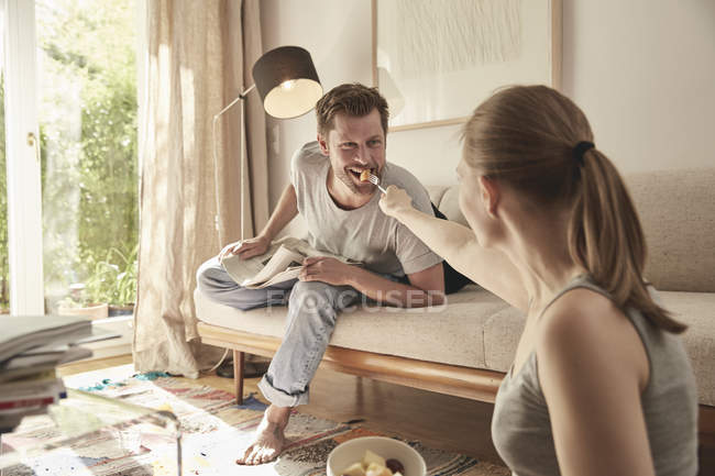 Donna che si nutre dell'uomo sul divano con frutta, scena casalinga — Foto stock