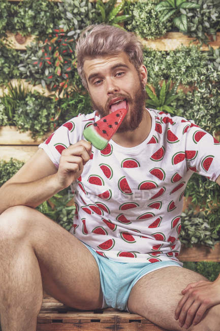 Porträt eines jungen Mannes, der Wassermeloneneis auf der Terrasse isst — Stockfoto