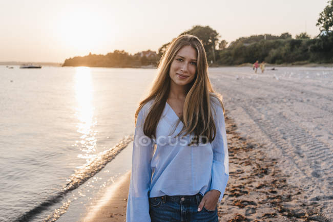 Sorridente giovane donna in piedi sulla spiaggia al crepuscolo — Foto stock