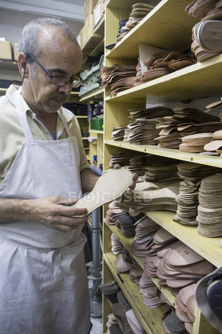 Обувщик выбирает подошвы для обуви с полки в своей мастерской — стоковое фото