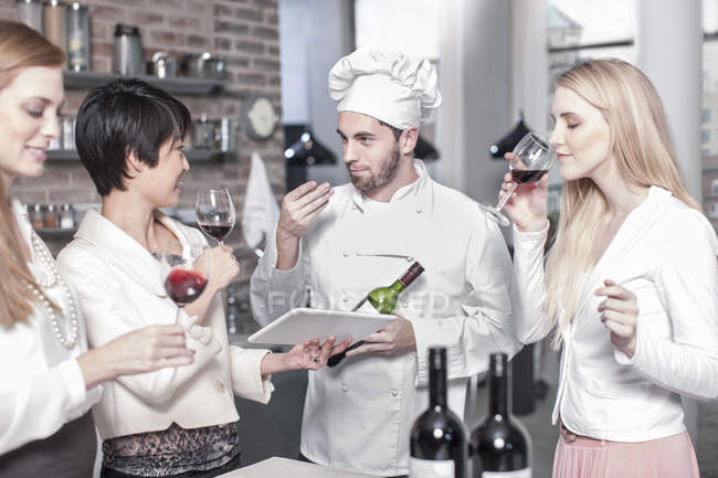 Chef con tre donne che degustano vino rosso in cucina — Foto stock