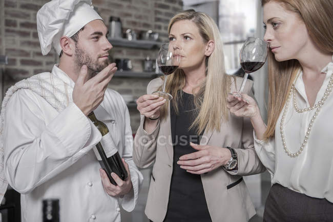 Chef con due donne in cucina degustazione vino — Foto stock