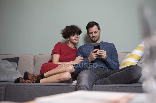 Paar sitzt zusammen auf Couch und teilt Handy — Stockfoto