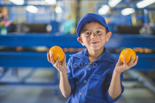 Little boy in orange farm warehouse holding oranges — Stock Photo