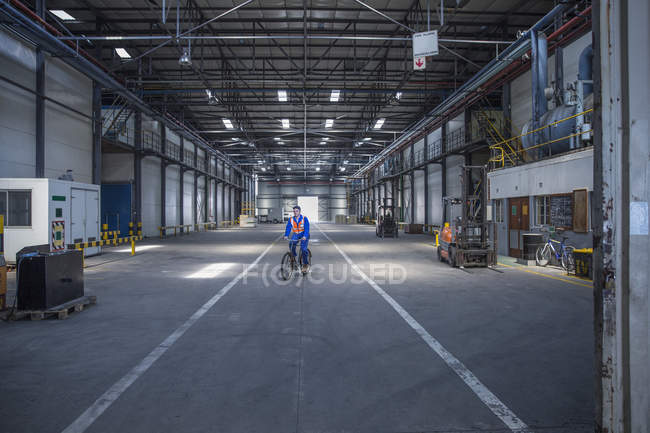 Arbeiter auf Fahrrad in Lagerhalle — Stockfoto
