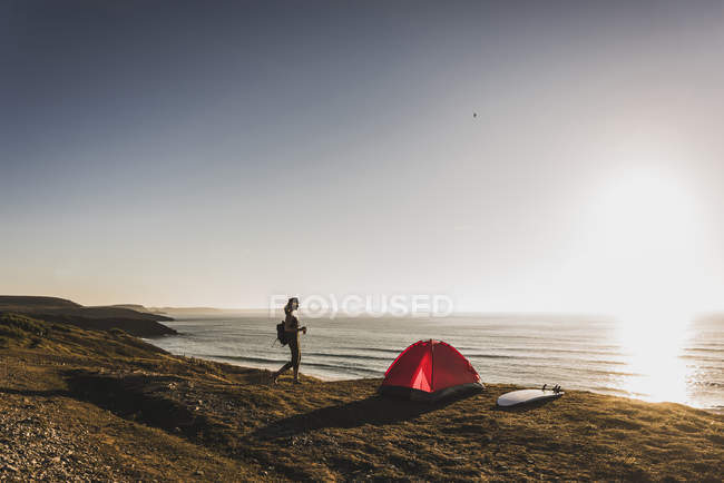 Adolescente avec tente rouge et planche de surf au bord de la mer au crépuscule du soir — Photo de stock