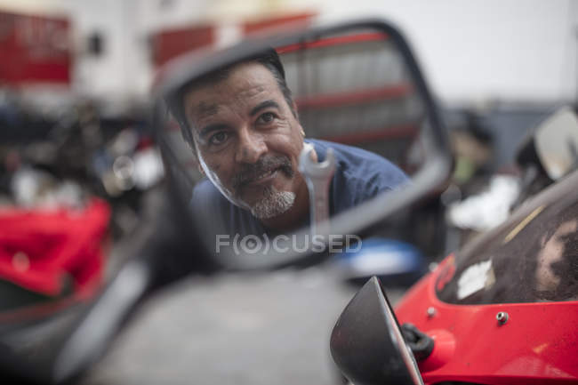 Motorcycle mechanic in workshop looking at rear-view mirror — Stock Photo