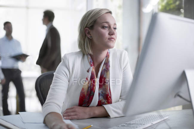 Жінка в кабінеті, сидячи за столом, дивлячись на комп'ютері — стокове фото