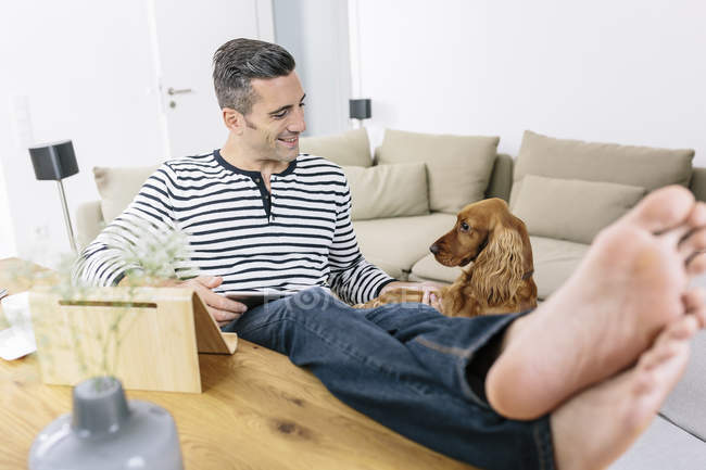 Relaxed man with dog at home using tablet — Stock Photo