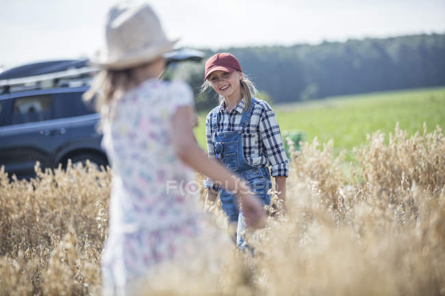 Zwei lachende Mädchen laufen in Feld mit Auto im Hintergrund — Stockfoto