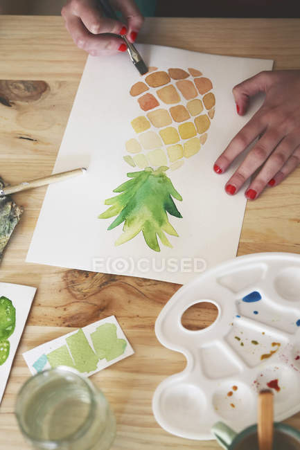 Женская рука рисует акварель ананаса за столом в своей студии — стоковое фото