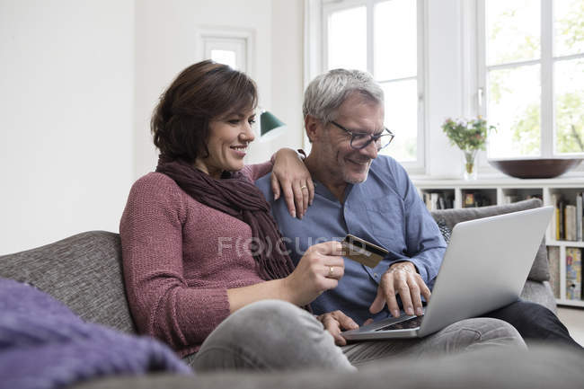 Smiling mature couple sitting on the sofa at home and shopping online — Stock Photo