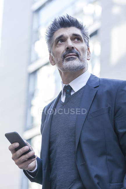 Бізнесмен стоїть з мобільним телефоном перед офісною будівлею — стокове фото