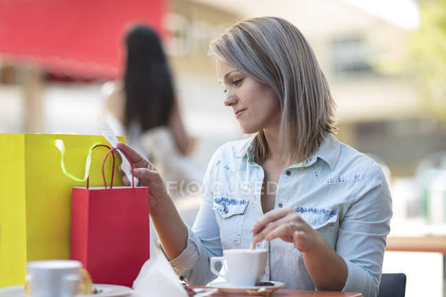 Female checking bill at city cafe square with shopping bags,having coffee — Stock Photo