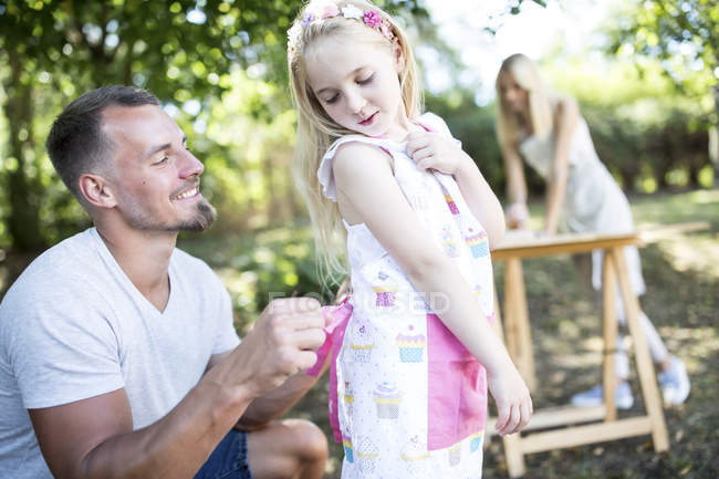 Father tying girls apron in garden — Stock Photo