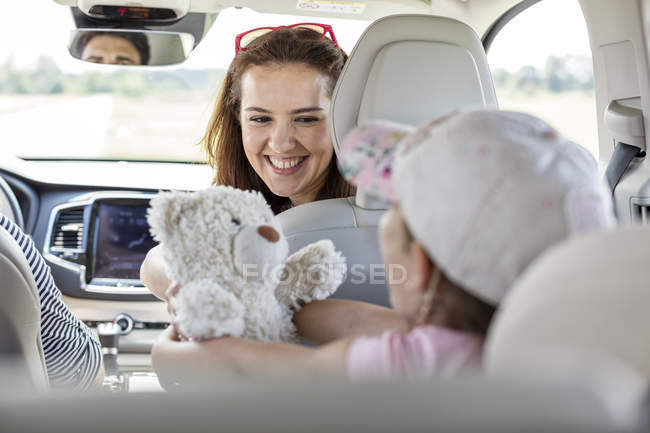 Madre e hija en viaje por carretera sentadas en el coche sosteniendo oso de peluche — Stock Photo