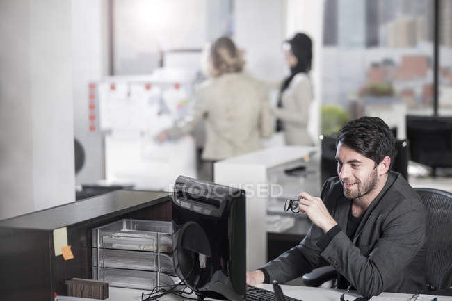Uomo d'affari sorridente seduto alla postazione di lavoro in ufficio — Foto stock