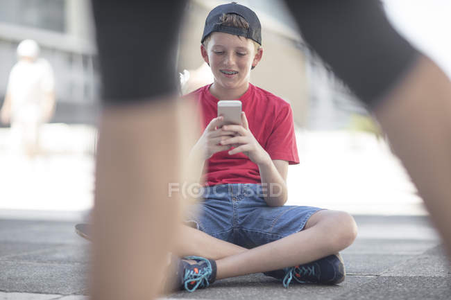 Хлопчик за допомогою смартфона сидячи, сидячи на скейтборді — стокове фото