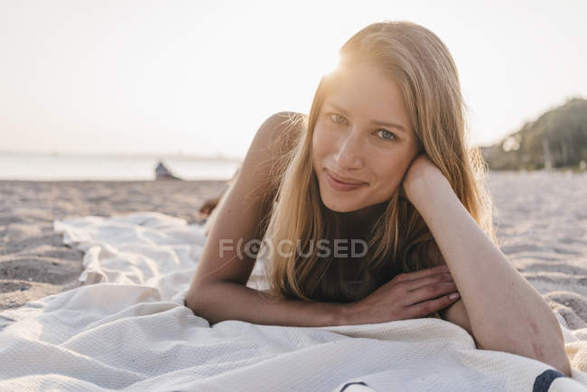 Porträt einer jungen Frau auf einer Decke am Strand liegend — Stockfoto