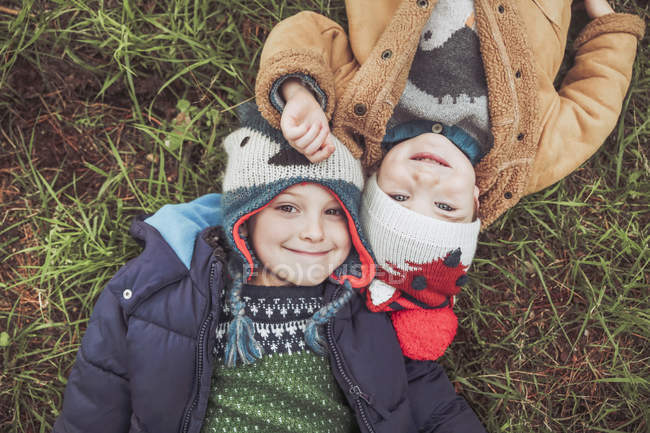 Two boys wearing wooly hats lying in grass — Stock Photo