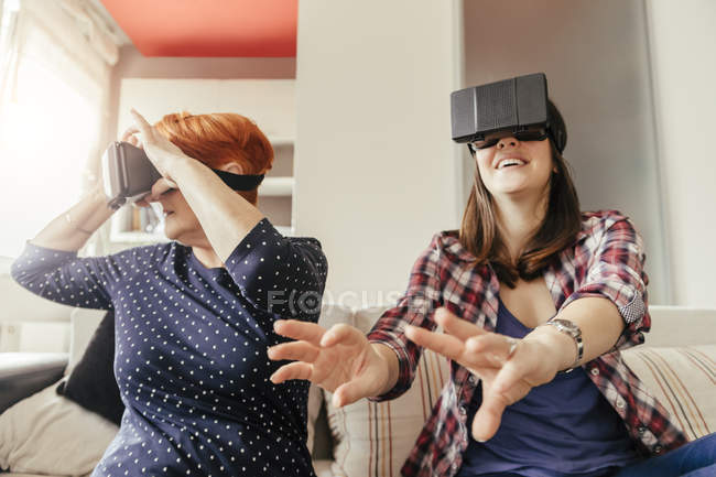 Madre e hija en gafas de realidad virtual sentadas en el sofá - foto de stock