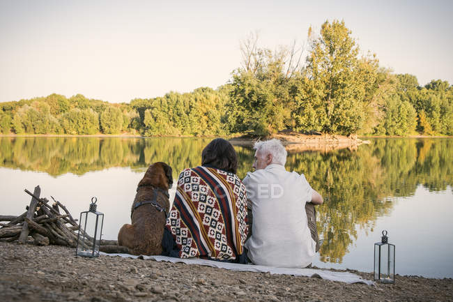 Расслабленная старшая пара с собакой на озере — стоковое фото