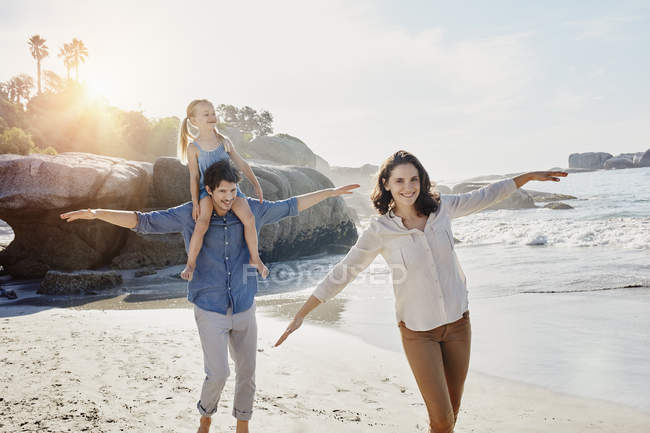 Счастливая семья гуляет с дочкой на пляже — стоковое фото
