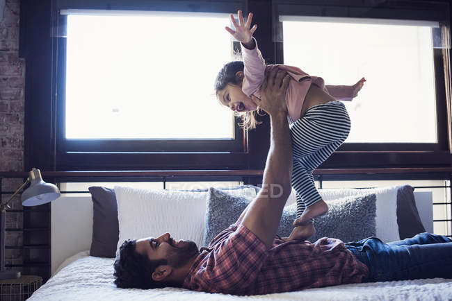 Батько, граючи з малюк дочка, лежачи на спині в спальні — стокове фото