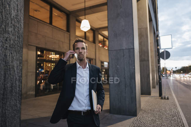 Retrato de hombre de negocios en el teléfono por la noche caminando en la ciudad - foto de stock